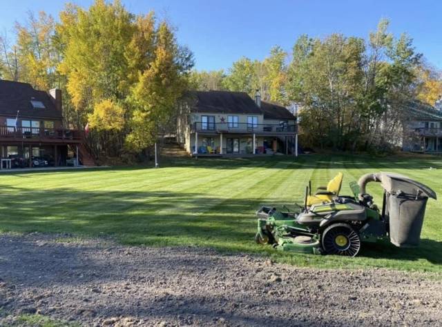 Zero-turn mower with a bagger on a striped lake lawn in the fall