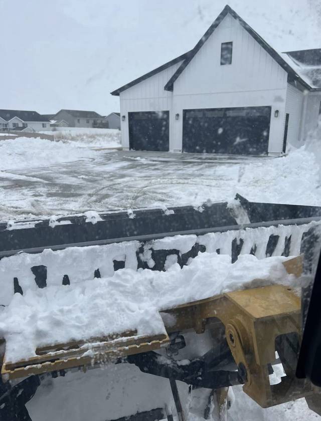 Skid steer with a snow pusher clearing a driveway