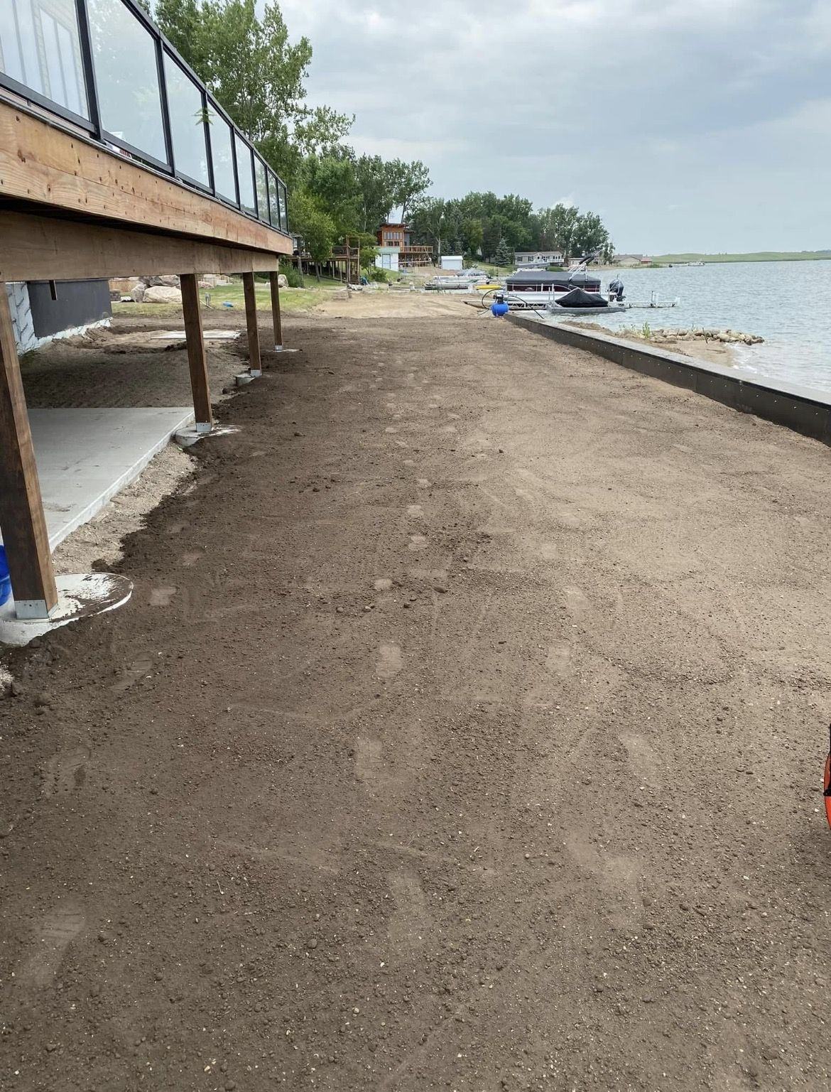 Bare graded dirt beside a lake home deck, ready for sod