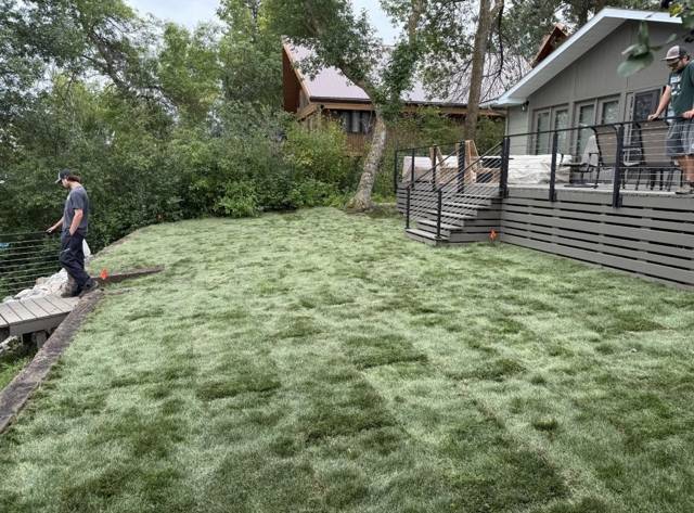 Crew checking freshly laid sod behind a lake home deck